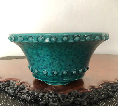 A teal glazed ceramic pot with raised bumps around rim and base.