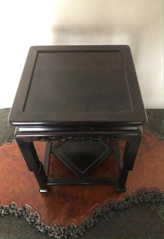 Dark wooden stand with square top and four legs, glossy finish, sits on patterned rug.
