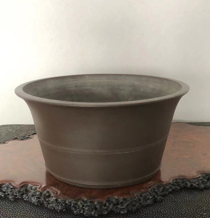 Dark grey matte ceramic pot with flared rim and two horizontal ridges, resting on a wooden tray.