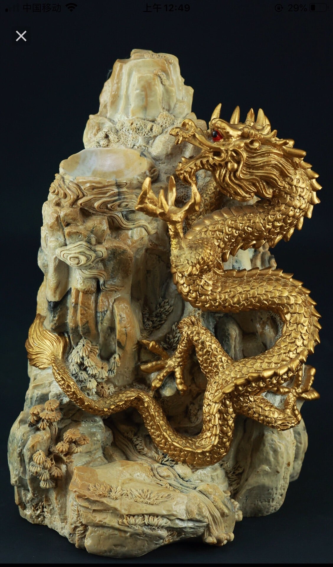 A golden dragon sculpture coils around a textured, light-colored rock formation with red eyes.