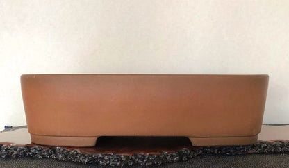 A matte, unglazed terracotta rectangular pot with a low foot, resting on a dark textured surface.