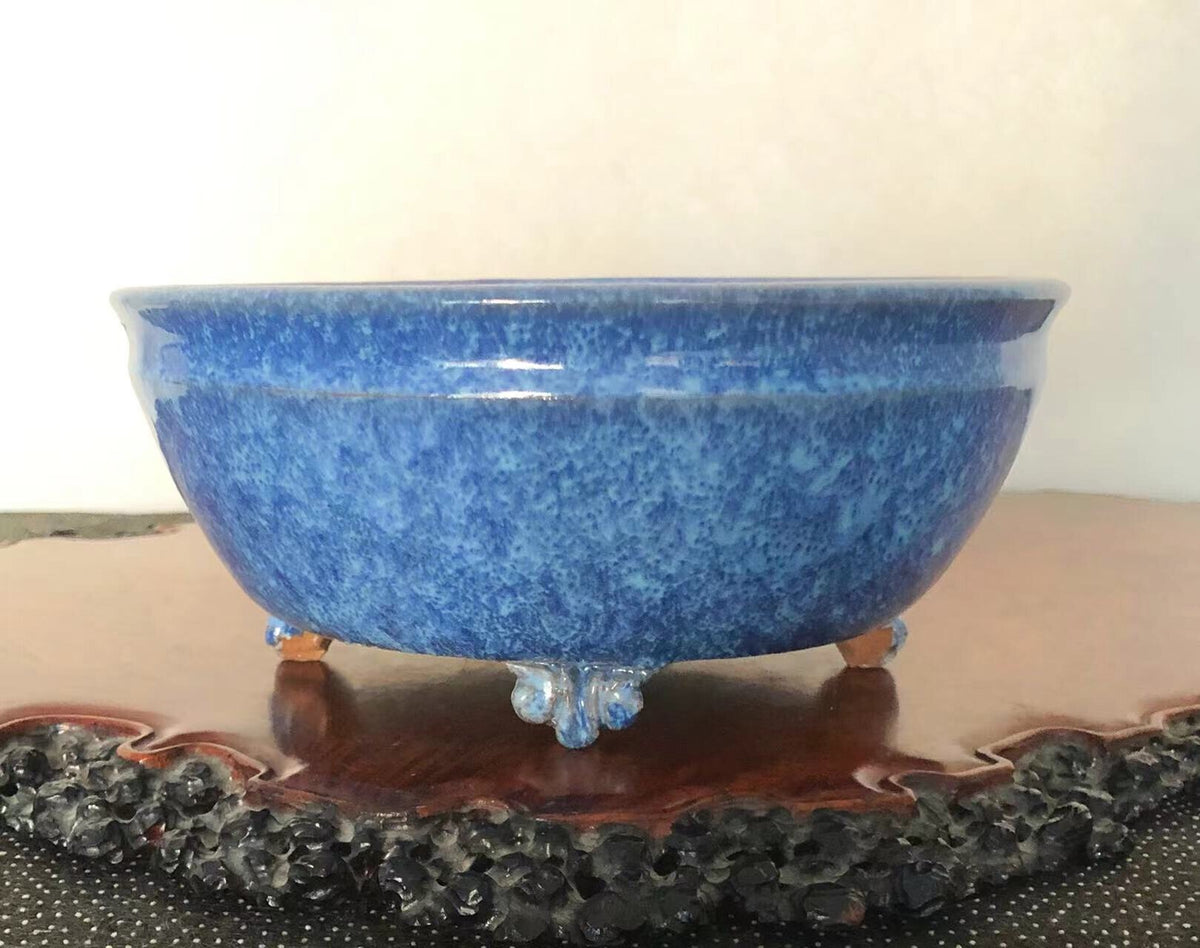 A glossy blue ceramic pot with speckled glaze, three ornate feet, and a wide rim.