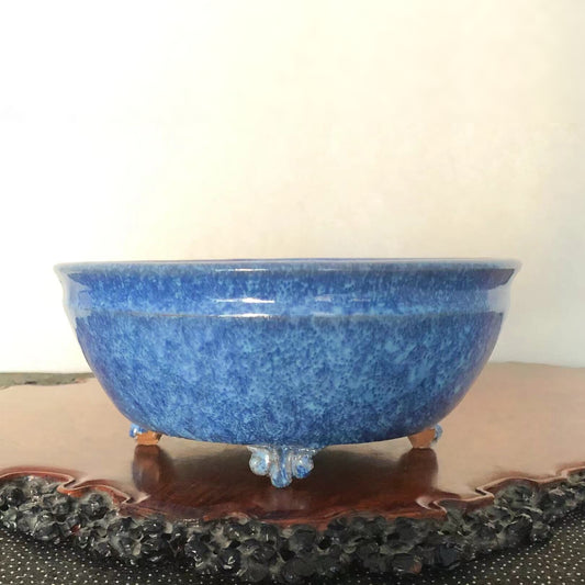 A glossy blue ceramic pot with speckled glaze, three ornate feet, and a wide rim.