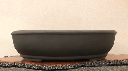 A matte black, oval-shaped pot with a low rim and unglazed surface.