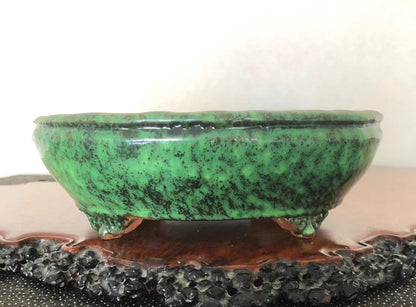 A glossy green ceramic pot with black speckles, resting on three small feet.