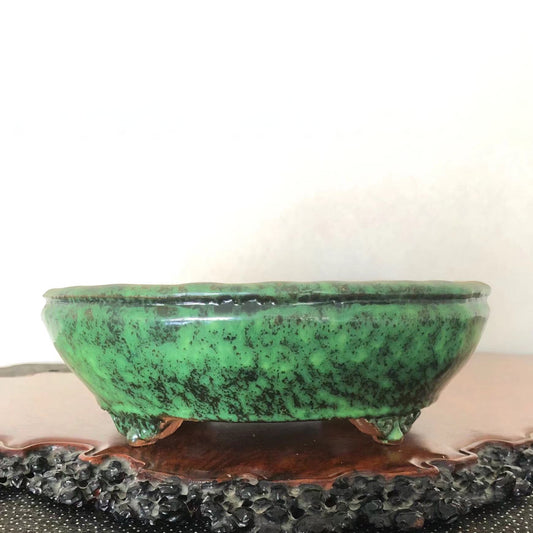 A glossy green ceramic pot with black speckles, resting on three small feet.