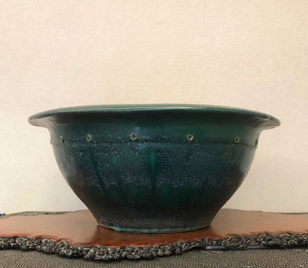 A wide, deep green glazed ceramic pot with speckled surface and small holes around rim.