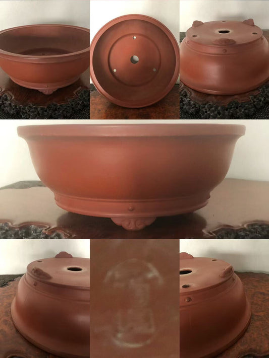 A reddish-brown unglazed ceramic bonsai pot with a wide rim, footed base, and drainage holes.