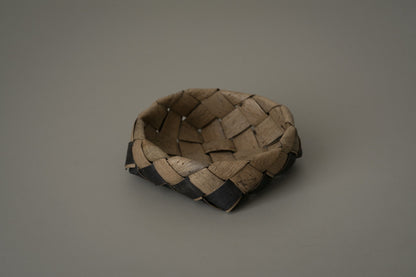 Small shallow box woven from strips of walnut bark in warm brown, on a plain grey ground.