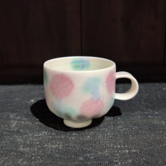 Cream ceramic mug with a small loop handle, hand-painted with soft pink, blue and green flower blooms.