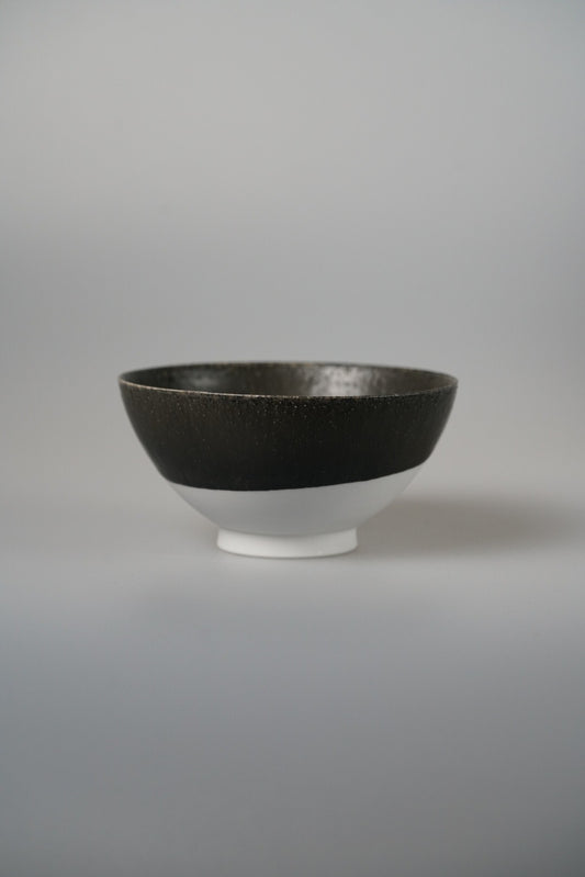 Footed bowl with a matte black upper half and a bright white foot, on pale grey.