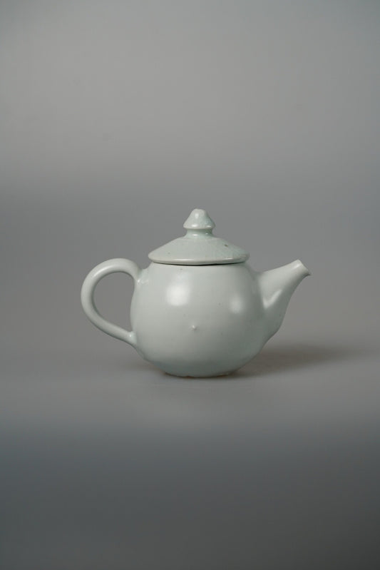 Small white porcelain teapot with a knopped lid, a short spout and a looping handle.