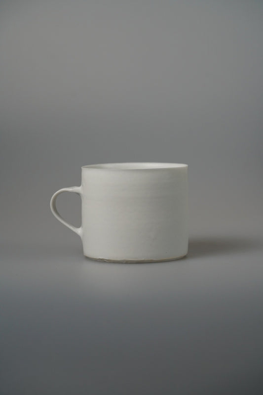Plain white mug with straight sides and a slim ring handle, on a pale grey ground.