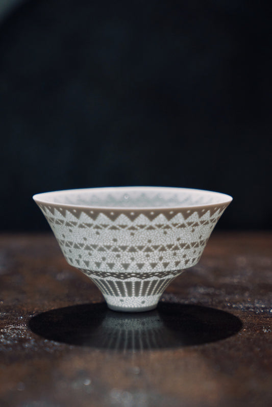Small conical white porcelain cup pierced with a fine lace band that glows where the light passes through.
