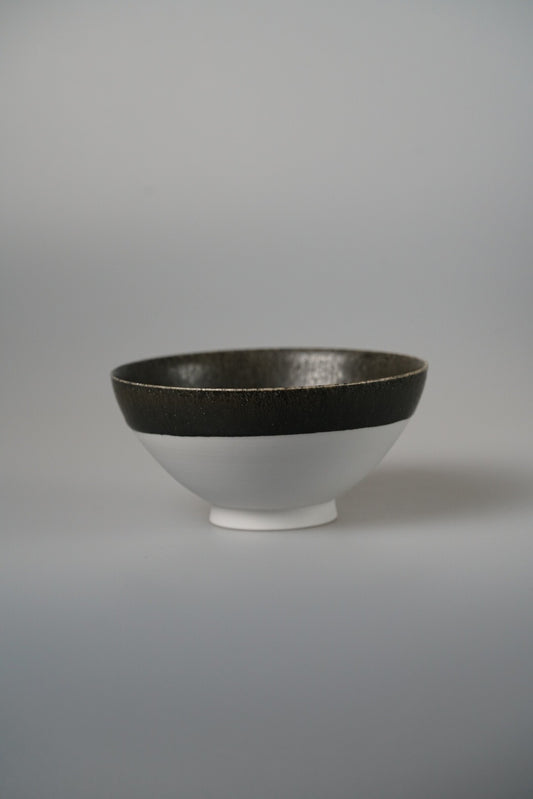 Shallow footed bowl with a speckled dark rim above a clean white lower body.