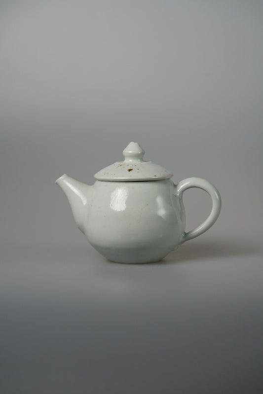 Small white porcelain teapot with a domed lid, slender spout and a curled handle.