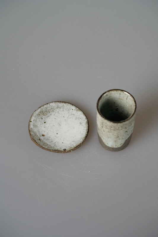 Small speckled green cup beside its matching pale saucer, on a pale grey ground.