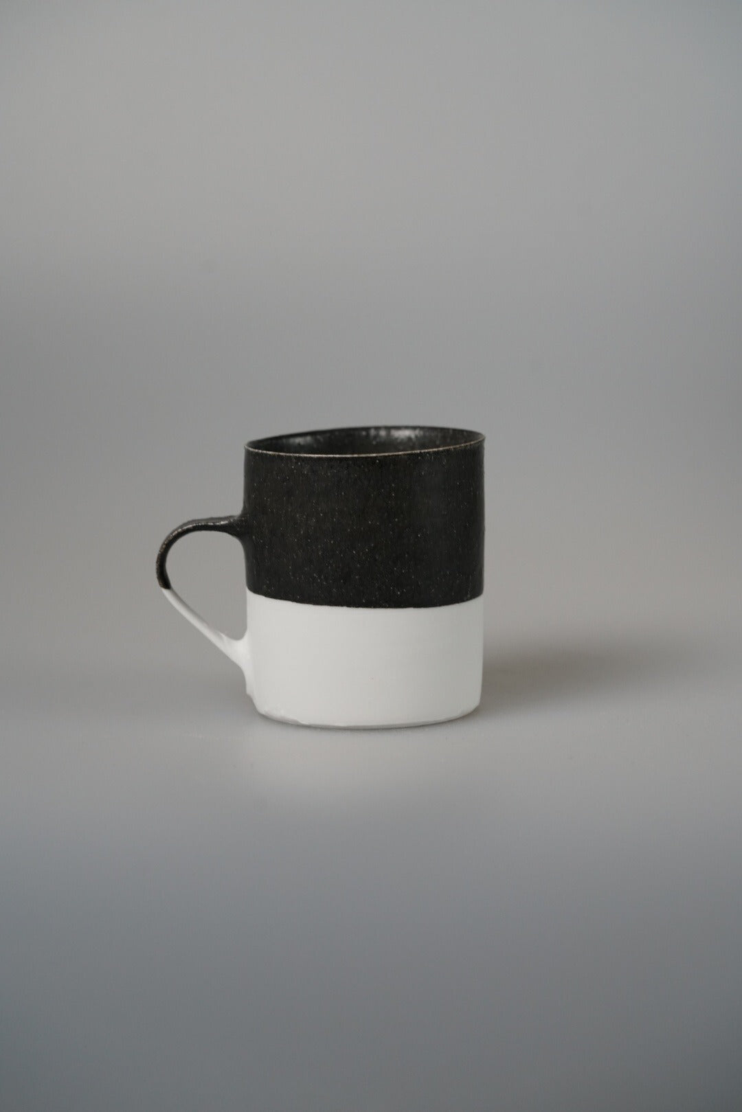 Tall mug with a matte black upper band over white, with a small dark ring handle.