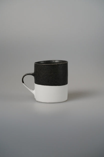 Tall mug with a matte black upper band over white, with a small dark ring handle.