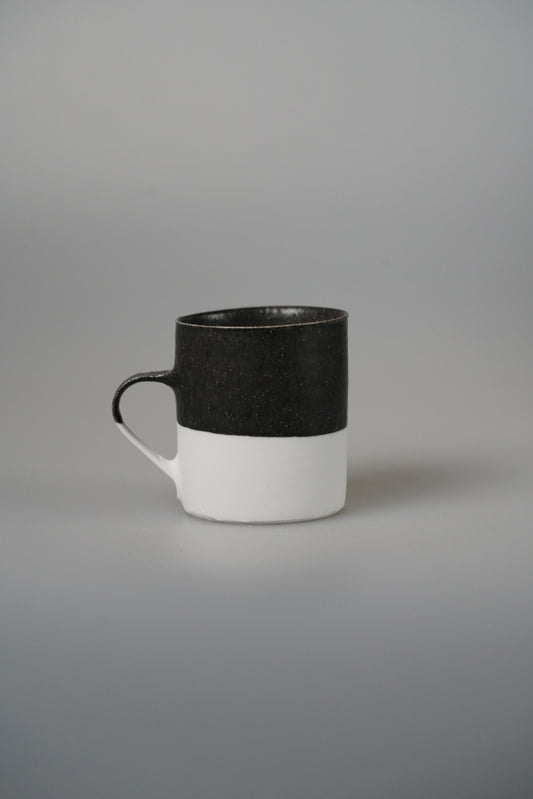 Tall mug with a matte black upper band over white, with a small dark ring handle.