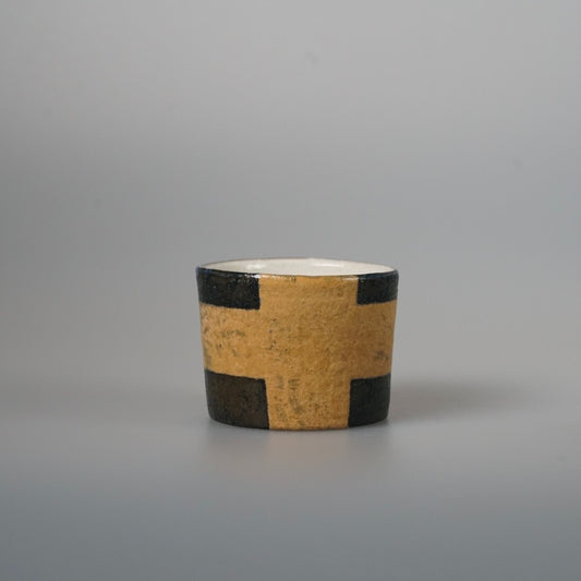 Straight-sided cup painted with a bold yellow and black check band, on pale grey.