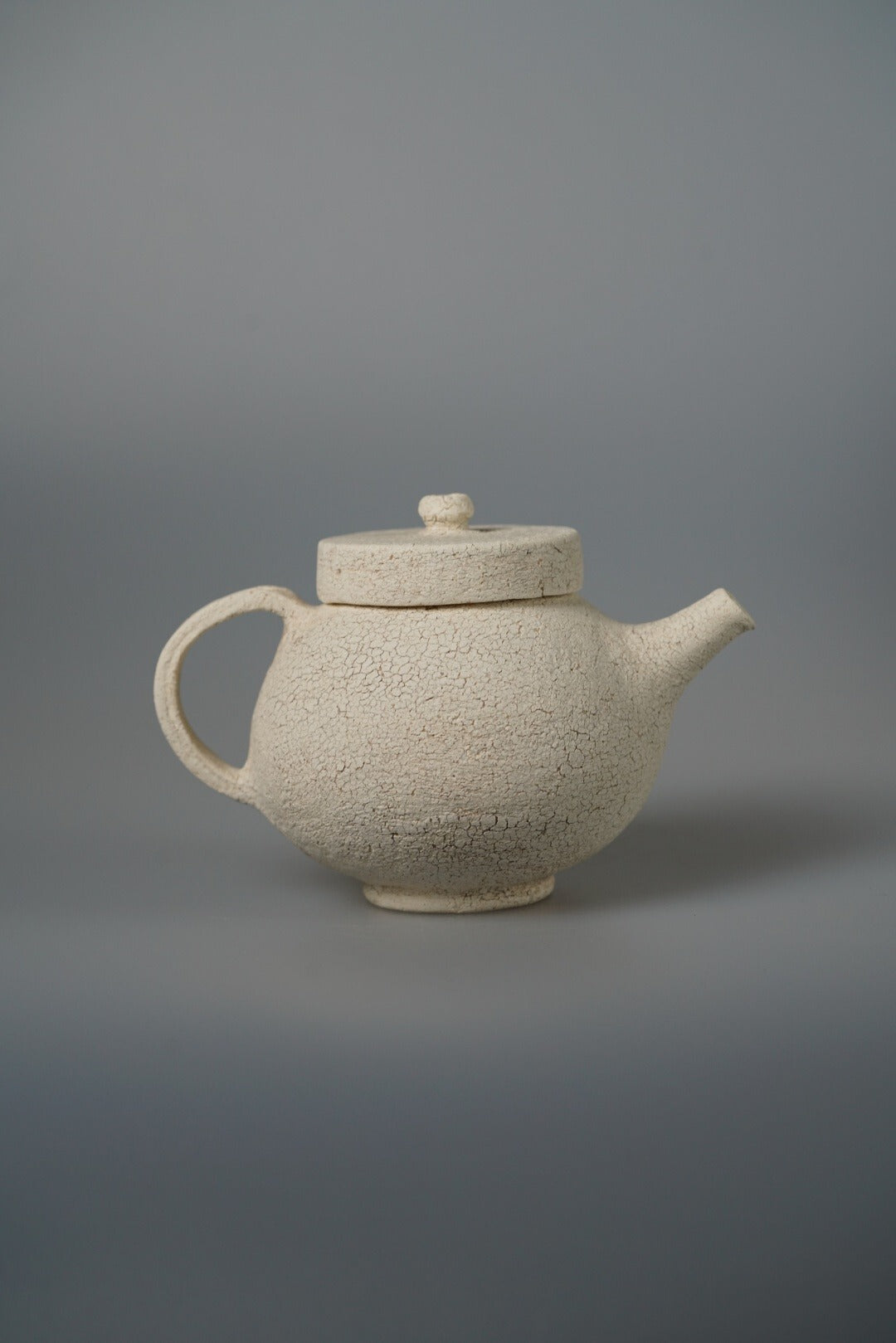 Cream teapot with a flat disc lid and a broad rounded body, on a pale grey ground.