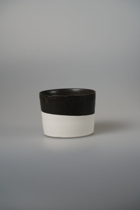 Small cup with a matte black upper band over a white lower body, on pale grey.