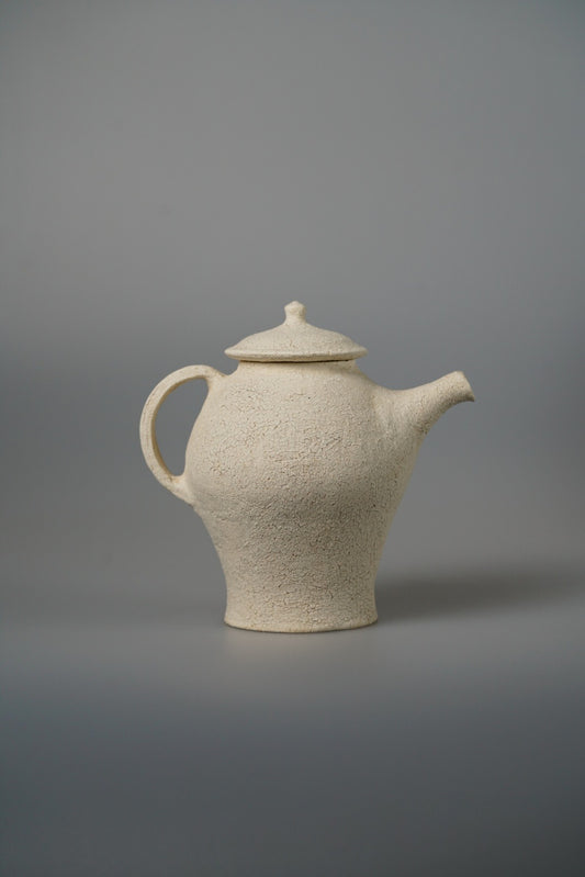 Tall cream teapot with a stepped waisted body, a pointed lid and a long spout.
