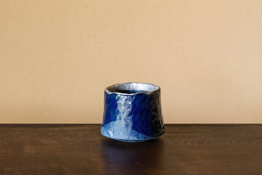 Small deep blue ceramic cup with a rough outer surface and a bright silver lining inside.