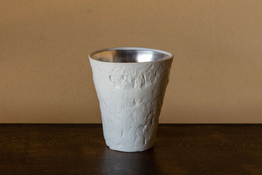 Tall white ceramic tumbler with a rough crumpled surface and a bright silver band around the rim.