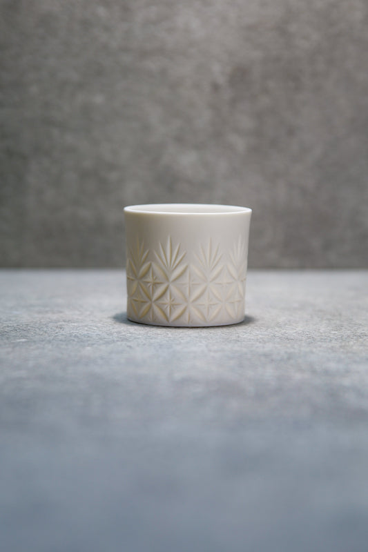 Small straight-sided white porcelain cup incised with a delicate starburst pattern.