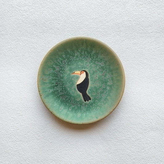 Small plate glazed in crackled sea green, painted at its centre with a black and white toucan.