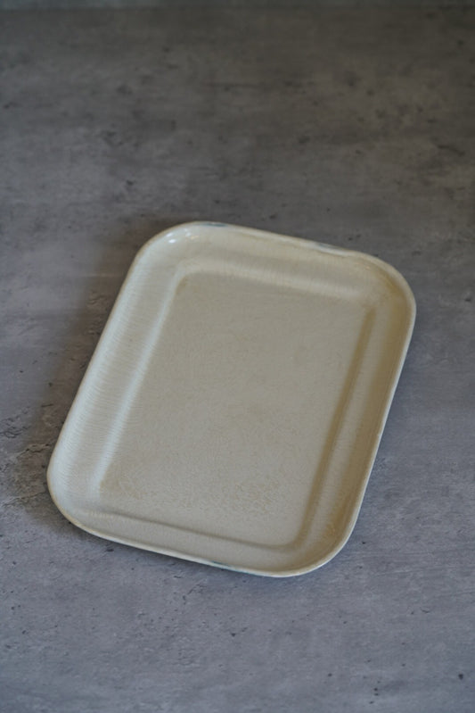 Rectangular white enamel tray with rounded corners and a low raised rim, on grey.