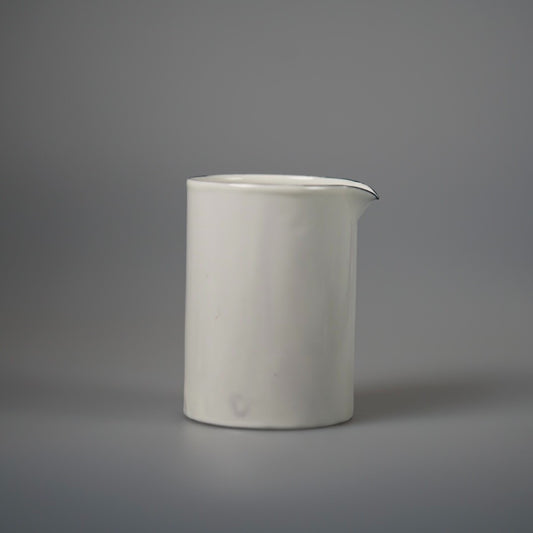 Tall cylindrical white enamel pourer with a small drawn lip, on a pale grey ground.