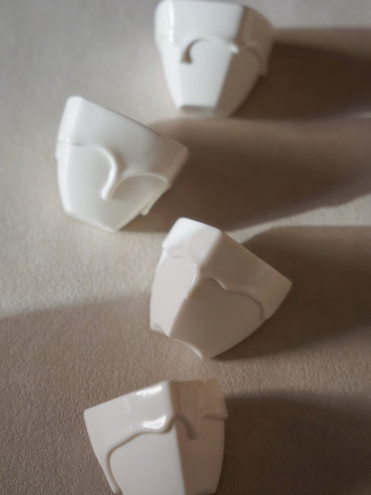 Four small white porcelain cups with soft folded rims that droop like poured milk, casting long shadows.