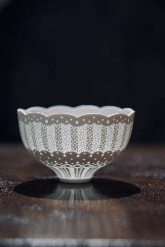 Footed white porcelain cup with a scalloped rim and a wide pierced lace band around its body.