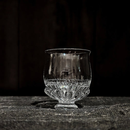 Small round footed glass cup with a band of fine lace-like texture around its lower half.