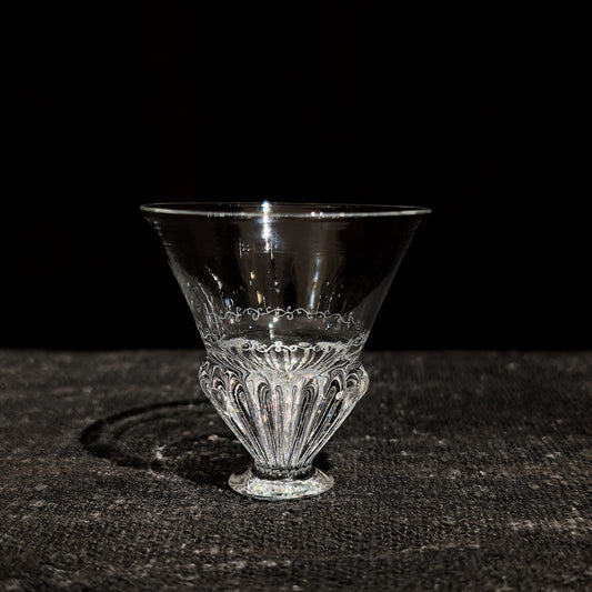 Small conical glass cup on a short stem, its ribbed base flaring into a smooth clear bowl.