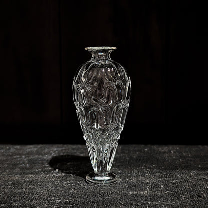 Slim clear glass vase with a narrow neck and a body cut in soft vertical ribs, on dark wood.