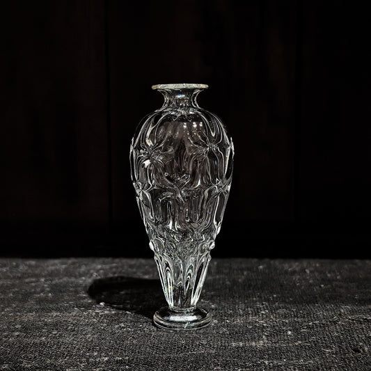 Slim clear glass vase with a narrow neck and a body cut in soft vertical ribs, on dark wood.