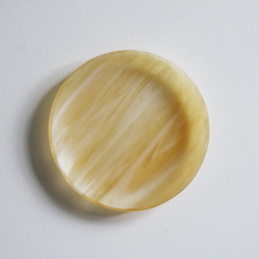 Round glass dish in warm amber and honey tones, its swirled bands catching the light.
