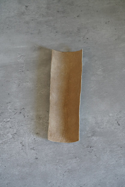 Curved strip of handmade washi paper in pale cream shading to warm brown, standing upright.