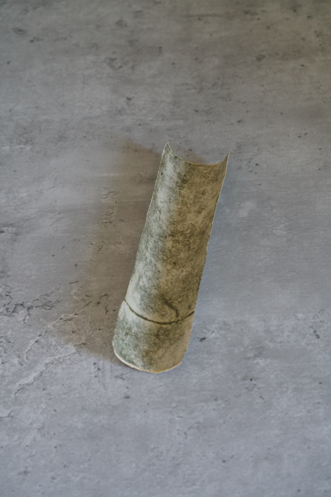 Curved strip of handmade washi paper in mottled green and grey, standing upright.