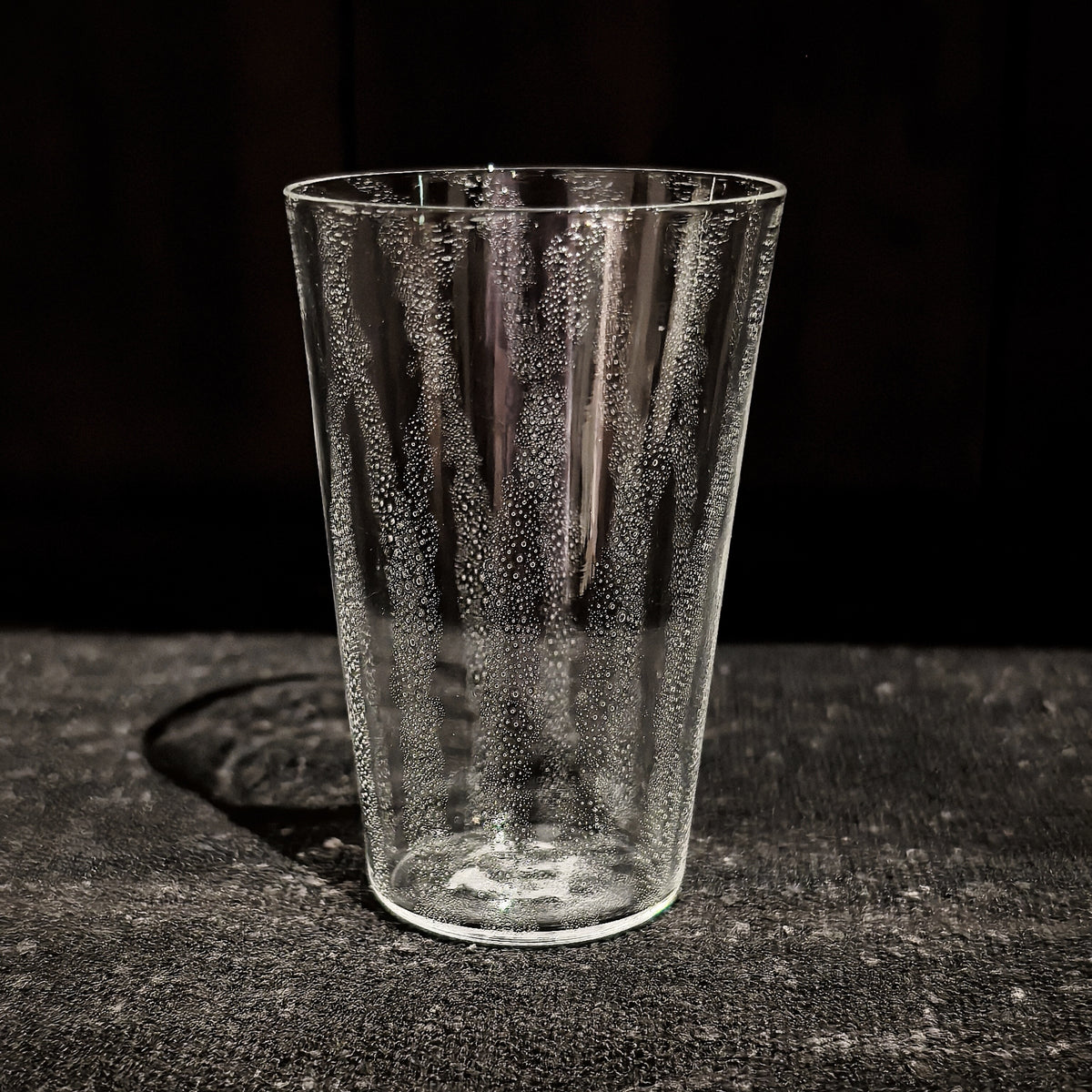 Tapered clear glass tumbler with a veil of tiny bubbles trapped through the glass.
